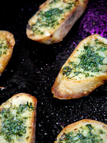 Herb buttered crostini spread out on a cast iron pan.