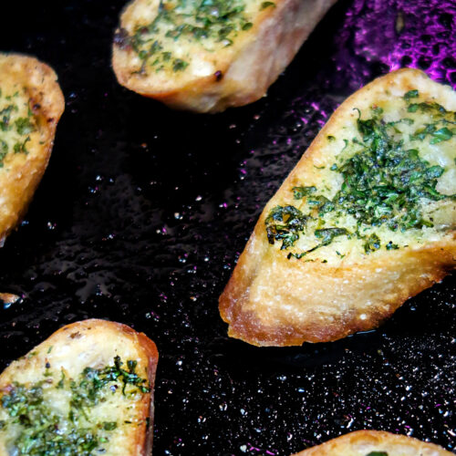Herb buttered crostini spread out on a cast iron pan.