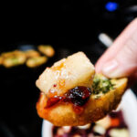 A hand holds a crostini with a chunk of brie and cranberry sauce piled on top.