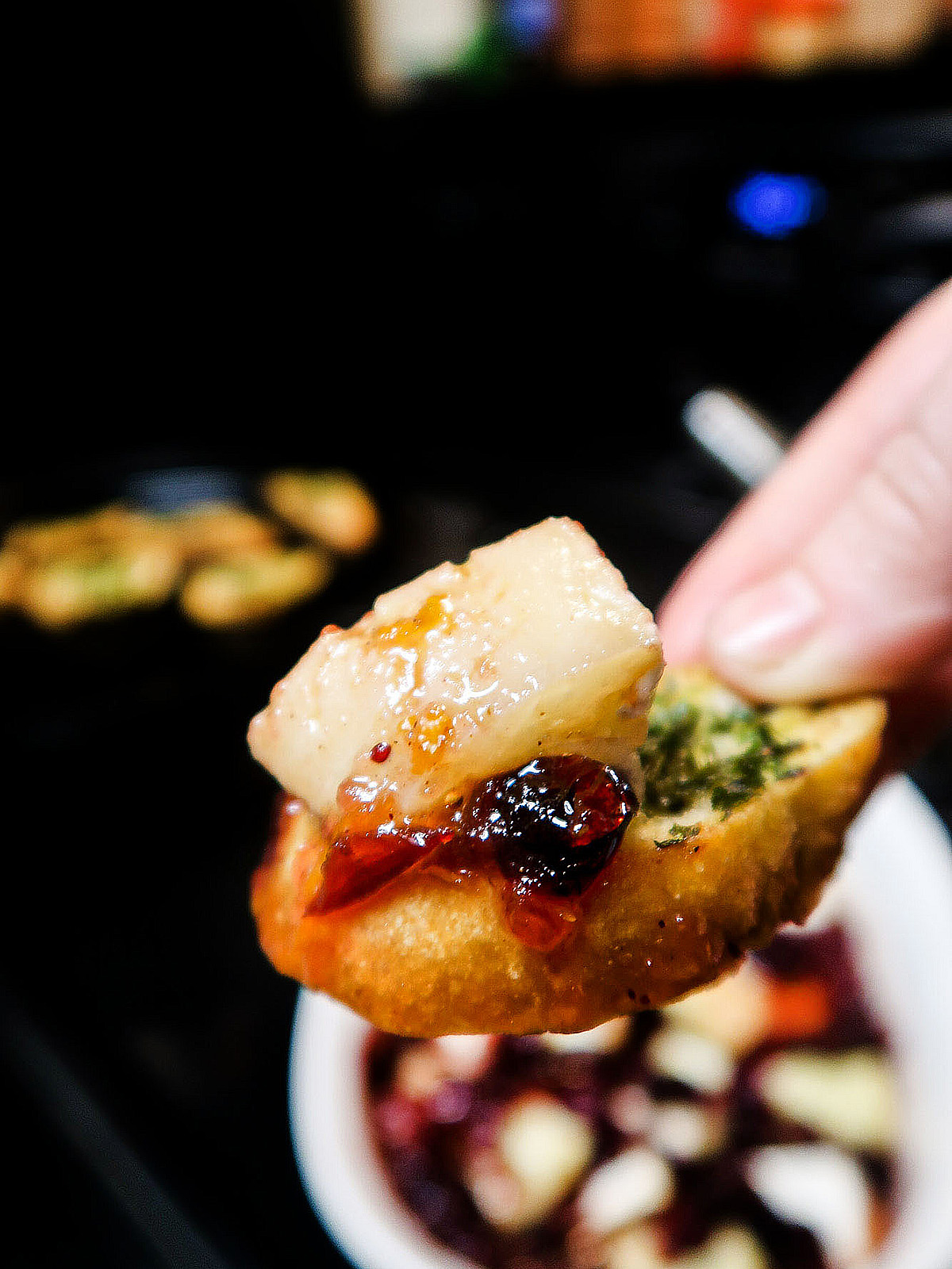 A hand holds a crostini with a chunk of brie and cranberry sauce piled on top.